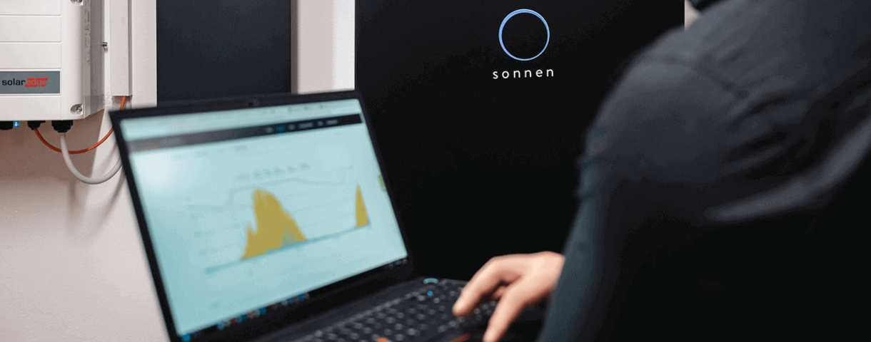 Person hält einen Laptop mit Grafik vor einem Sonnenspeicher